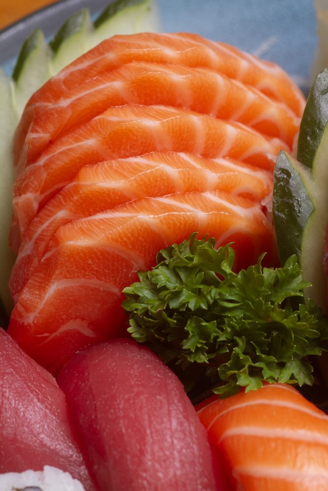 Close de lâminas de salmão fresco cortadas para sashimi, com salsinha e pepino